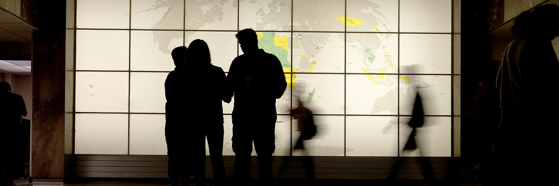 Three people are silhouetted in front of a world map.