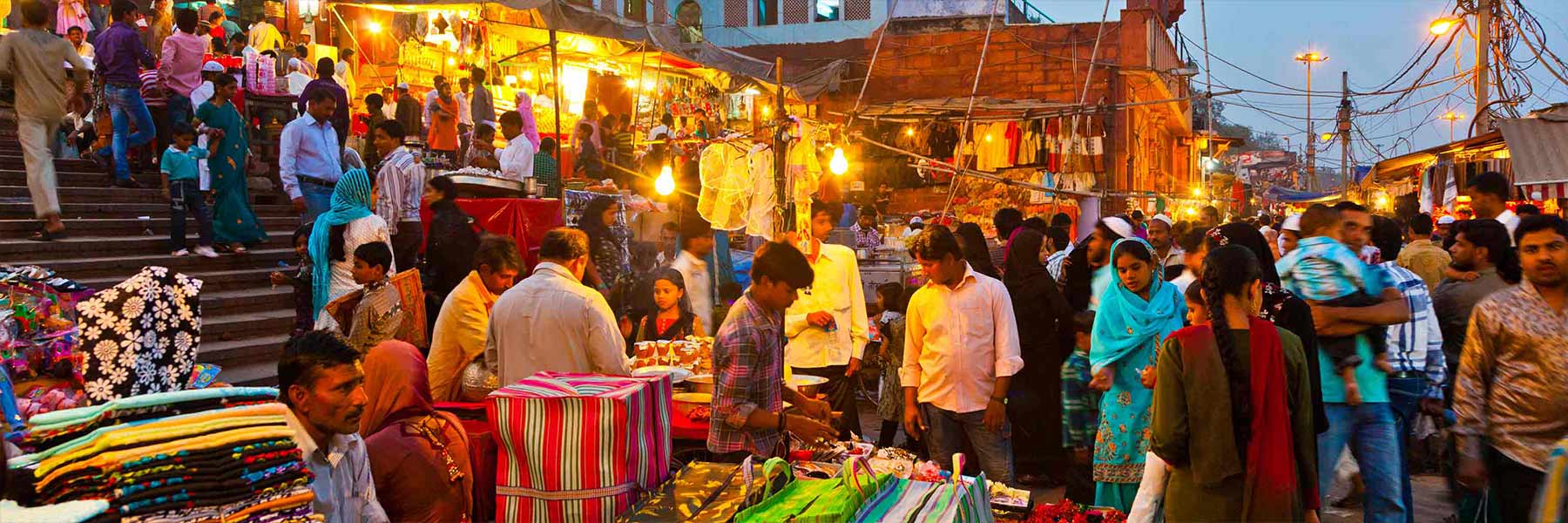 Shoppers browse at an outdoor market at dusk.