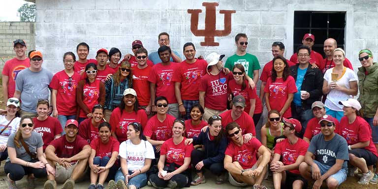 A group stands in front of a wall painted with the IU trident.
