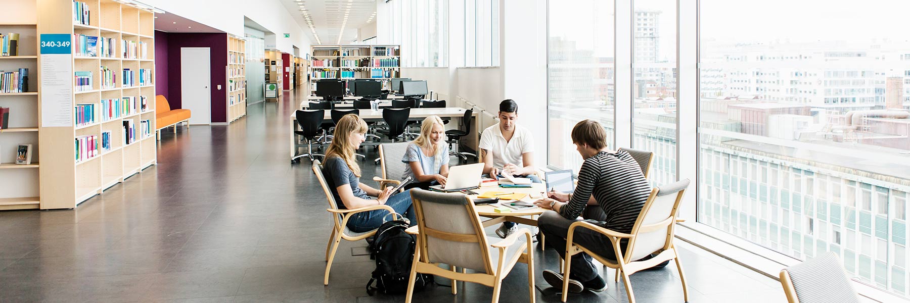Students work around a table in a brightly lit library.